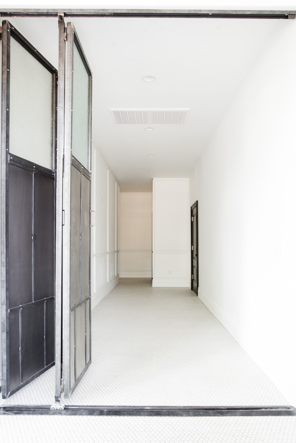 Wide hallway with white hexagon floor tile and heavy steel folding doors 
