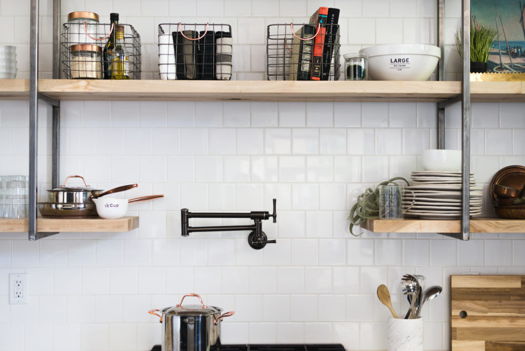 White square subway tile with white grout and open shelving with raw steel brackets make this renovation a vintage lovers dream! You've got to see the rest of the kitchen! (It has green cabinetry!)